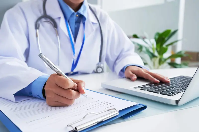Médica preenchendo um atestado ao lado do notebook